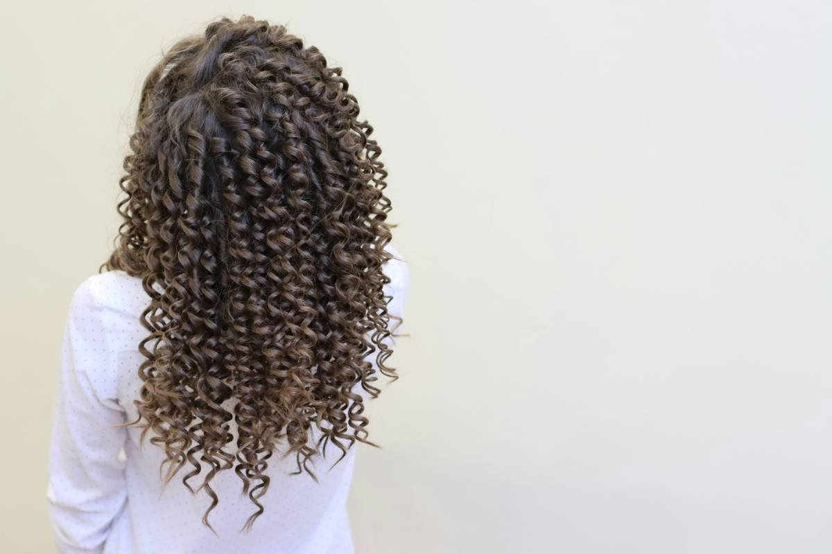 Woman applying frizz taming styling cream to damp hair in bathroom mirror