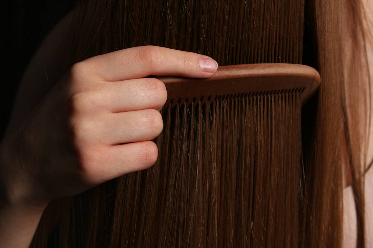 Woman applying hair treatment smooth product to damp hair in bathroom